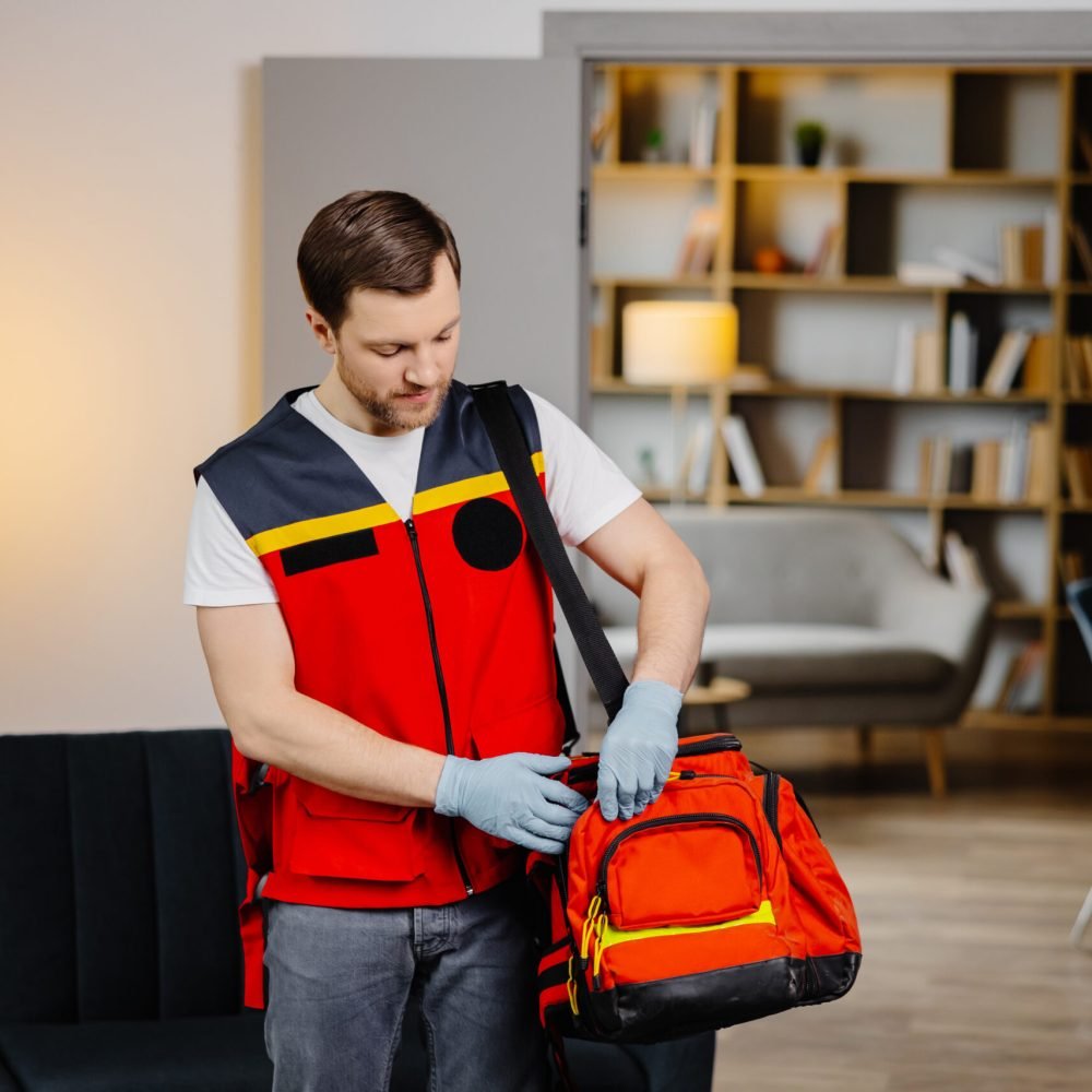 First aid course. A young male paramedic with a bag on his shoulders is standing in a classroom before a lecture.