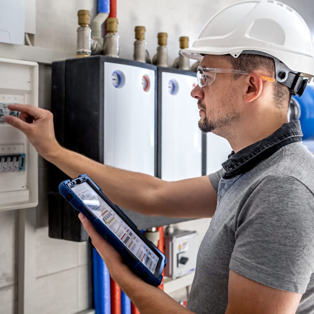 Man, an electrical technician working in a switchboard with fuses. Installation and connection of electrical equipment. Professional uses a tablet.