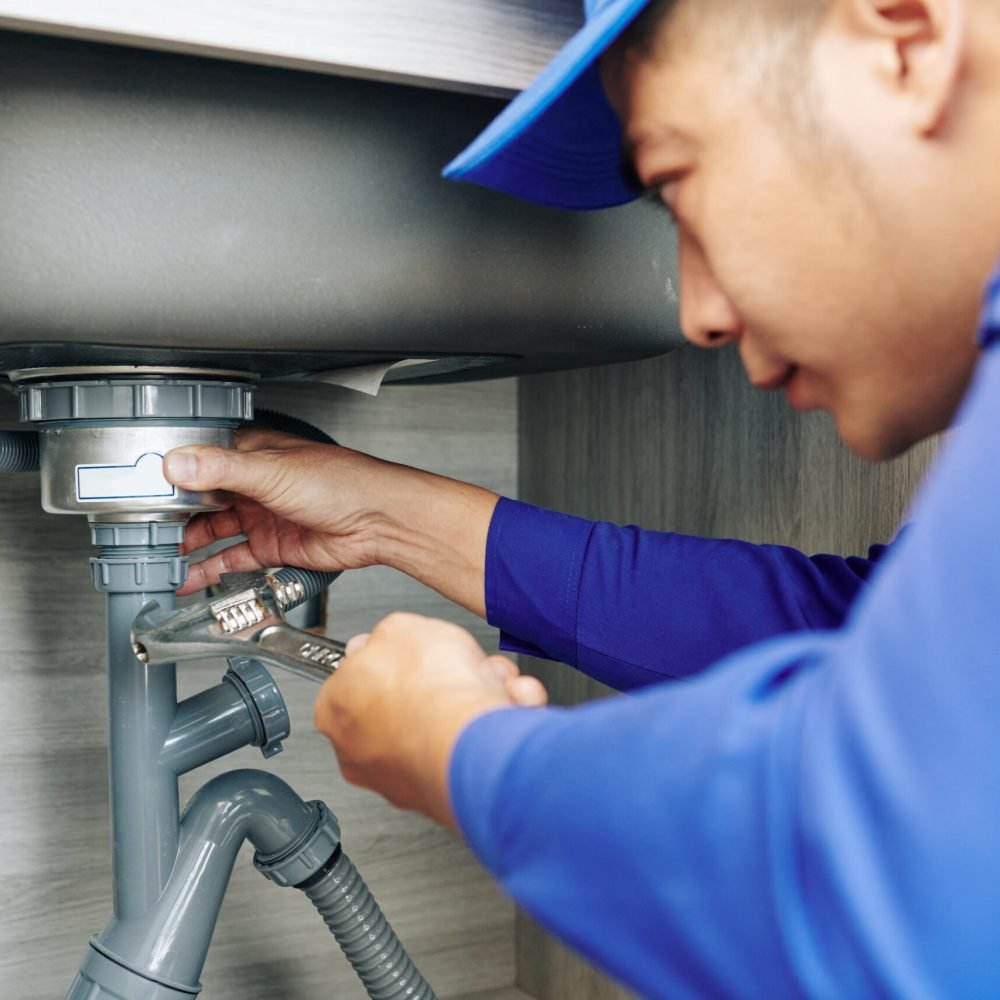 Serious plumber using wrench when repairing leaky drain in kitchen